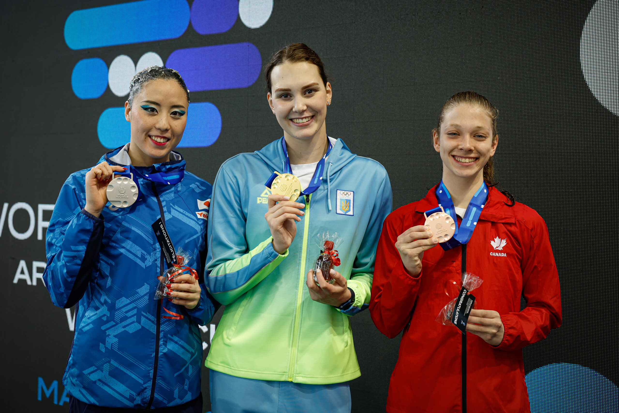 Trois nageuses artistiques souriantes sur le podium.