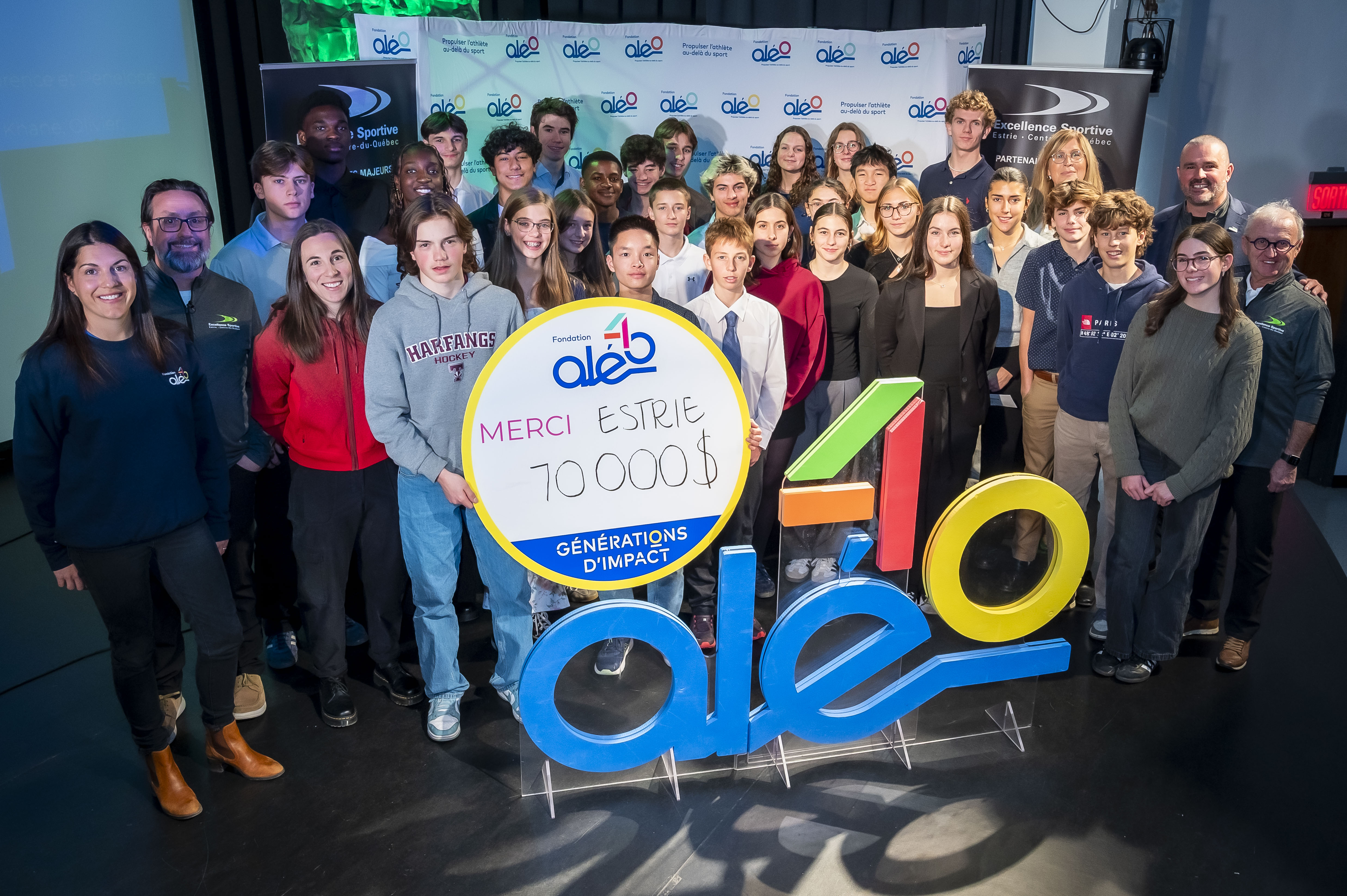 Récipiendaires des bourses régionales en Estrie en compagnie de Véronique Boudreault (1re à gauche), titulaire de la Chaire de recherche Aléo, Patrice Henrichon (2e à gauche), coanimateur de l’événement, Lauriane Genest (chandail rouge), médaillée olympique et boursière Aléo, Patricia Demers (en haut à droite), directrice générale de la Fondation Aléo, Rémy Fontaine (2e à droite), directeur général d'Excellence Sportive Sherbrooke, et Jacques Petit (1er à droite), ancien directeur général d'Excellence Sportive Sherbrooke. (photo Jessica Garneau)